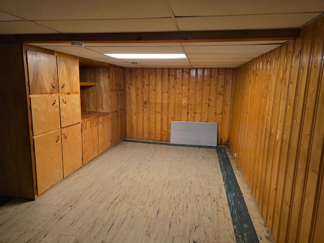 basement featuring a paneled ceiling and wood walls