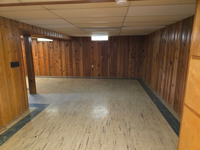 basement featuring a paneled ceiling and wooden walls