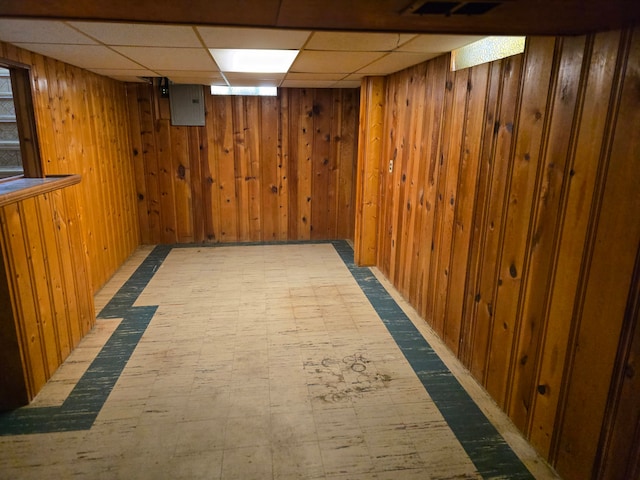 basement featuring a paneled ceiling and wooden walls