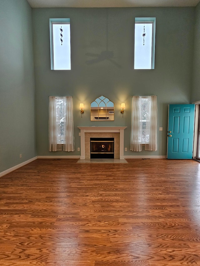 unfurnished living room with a healthy amount of sunlight, hardwood / wood-style floors, a fireplace, and a towering ceiling