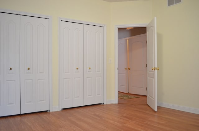 unfurnished bedroom featuring two closets and light wood-type flooring