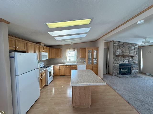 kitchen with lofted ceiling with skylight, sink, light wood-type flooring, a kitchen island, and white appliances