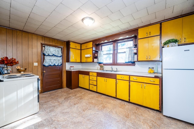 kitchen featuring white appliances, washer / clothes dryer, sink, and wood walls