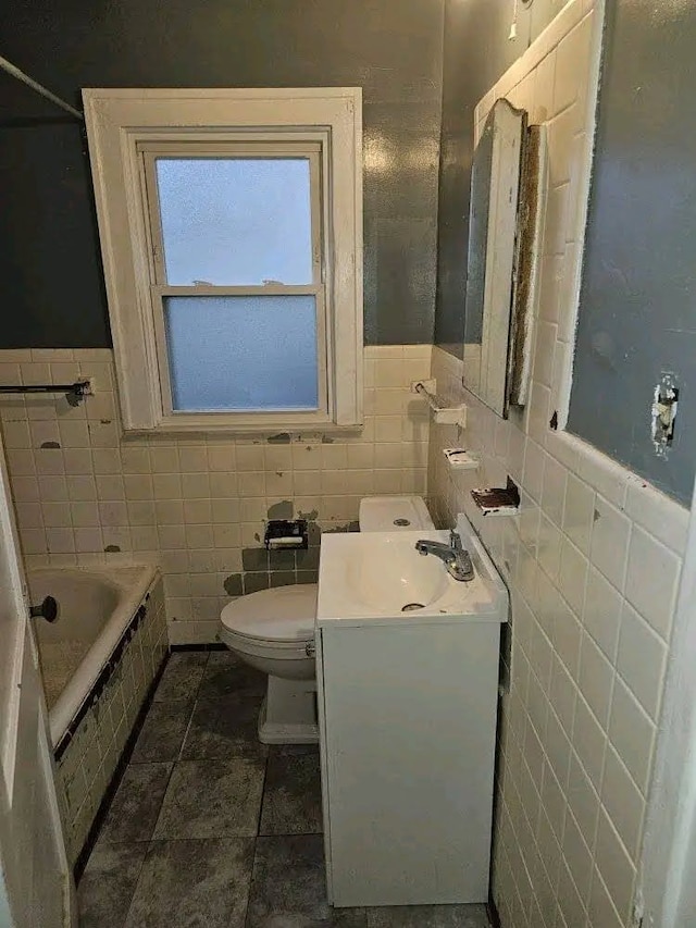 bathroom with tiled tub, vanity, tile walls, and toilet