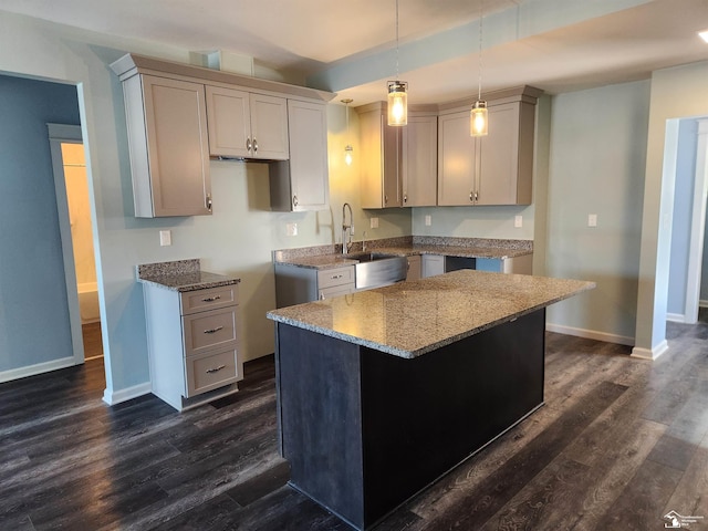 kitchen with hanging light fixtures, light stone countertops, a kitchen island, and sink