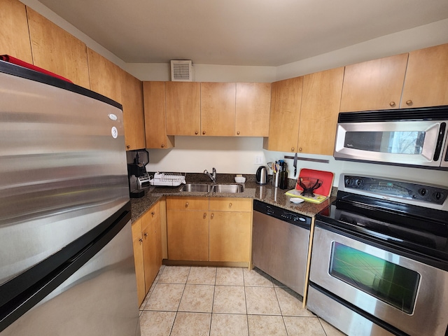 kitchen featuring stainless steel appliances, dark stone countertops, sink, and light tile patterned floors