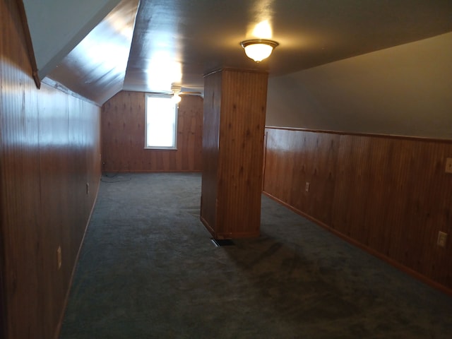 additional living space featuring dark colored carpet, vaulted ceiling, and wood walls