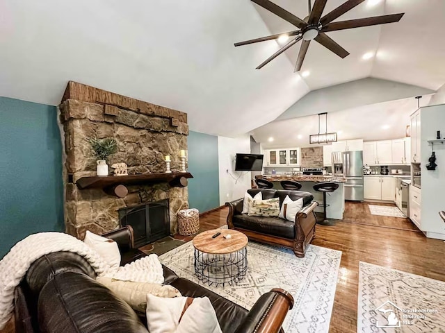 living room featuring vaulted ceiling, a stone fireplace, ceiling fan, and light wood-type flooring