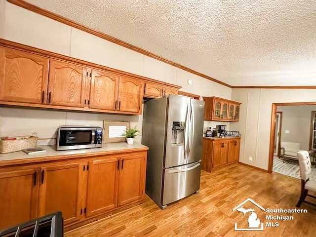 kitchen featuring ornamental molding, appliances with stainless steel finishes, a textured ceiling, and light wood-type flooring