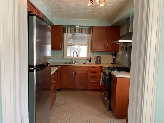 kitchen featuring wall chimney range hood, light tile patterned floors, stainless steel appliances, and sink