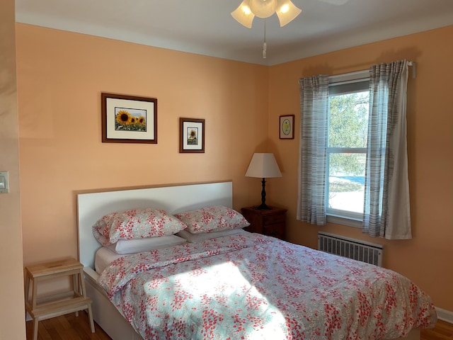 bedroom with hardwood / wood-style flooring, radiator, ceiling fan, and multiple windows