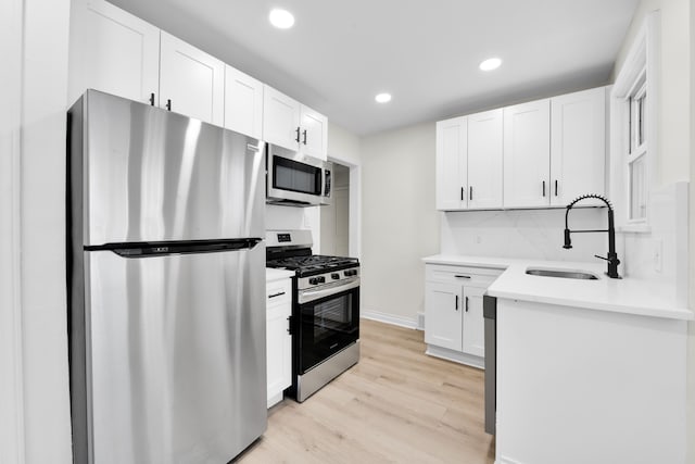 kitchen with sink, stainless steel appliances, white cabinets, decorative backsplash, and light wood-type flooring