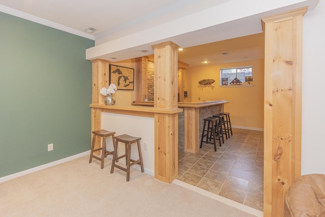 kitchen featuring a breakfast bar area, ornamental molding, light brown cabinetry, light colored carpet, and kitchen peninsula