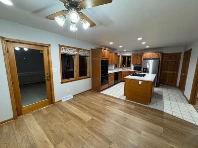 kitchen with sink, ceiling fan, a center island, black appliances, and light wood-type flooring