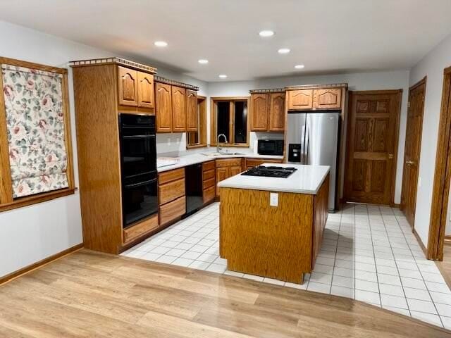 kitchen with light hardwood / wood-style floors, sink, a kitchen island, and black appliances