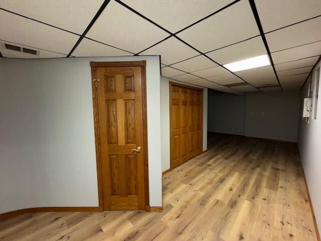 basement with a paneled ceiling and light wood-type flooring