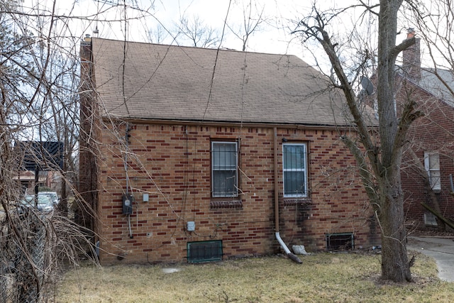 view of side of home with a shingled roof, brick siding, and a chimney