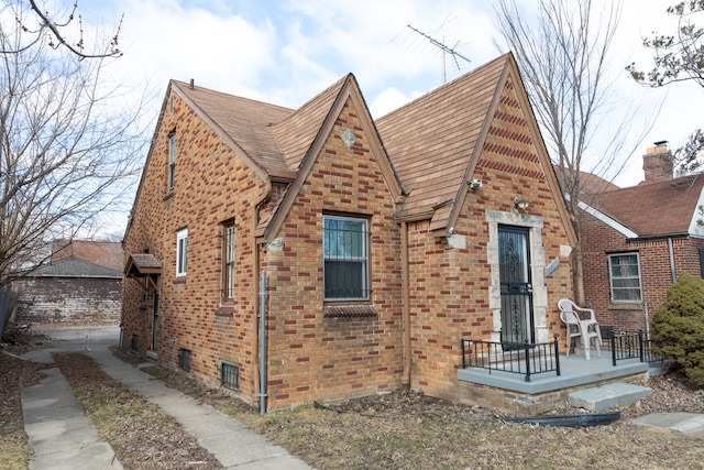 tudor-style house featuring brick siding and roof with shingles