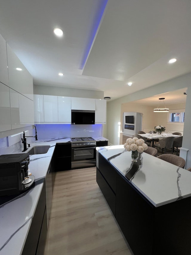 kitchen featuring sink, gas range, white cabinetry, hanging light fixtures, and light wood-type flooring