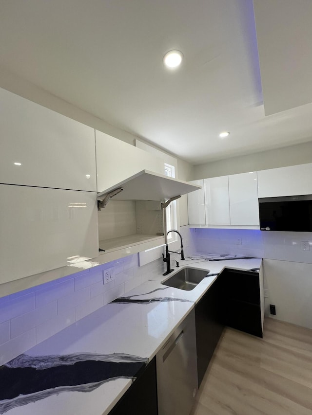 kitchen featuring sink, white cabinets, stainless steel dishwasher, light stone countertops, and light wood-type flooring