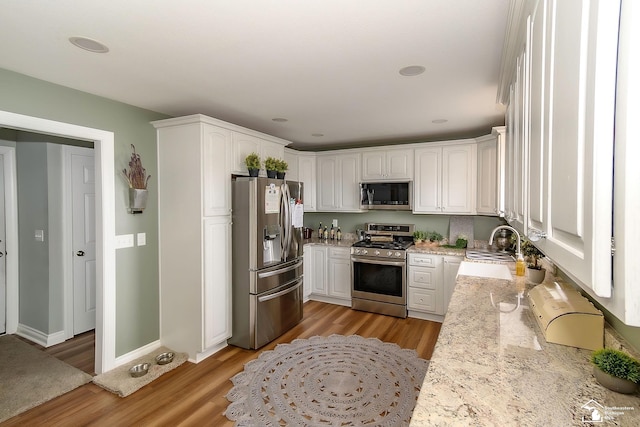 kitchen with appliances with stainless steel finishes, sink, white cabinets, light hardwood / wood-style floors, and light stone countertops