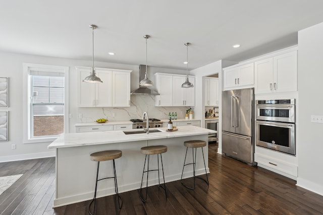 kitchen featuring white cabinetry, appliances with stainless steel finishes, pendant lighting, and wall chimney range hood