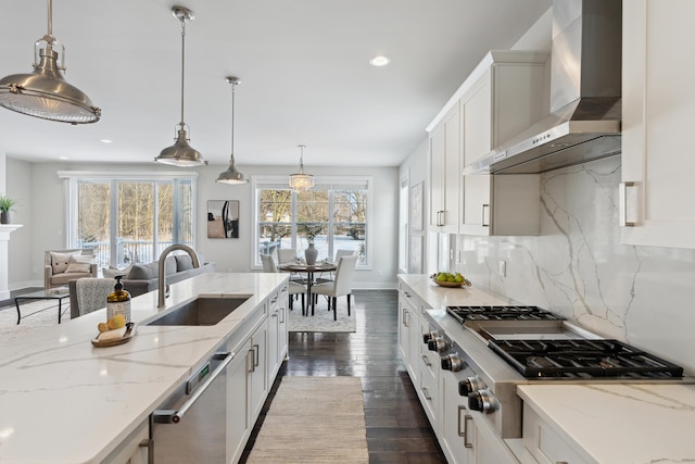 kitchen with decorative light fixtures, white cabinetry, sink, backsplash, and wall chimney exhaust hood