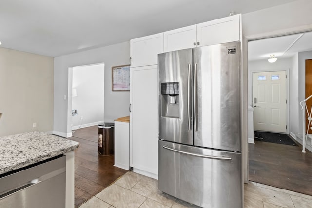 kitchen with appliances with stainless steel finishes, light stone countertops, light tile patterned floors, and white cabinets