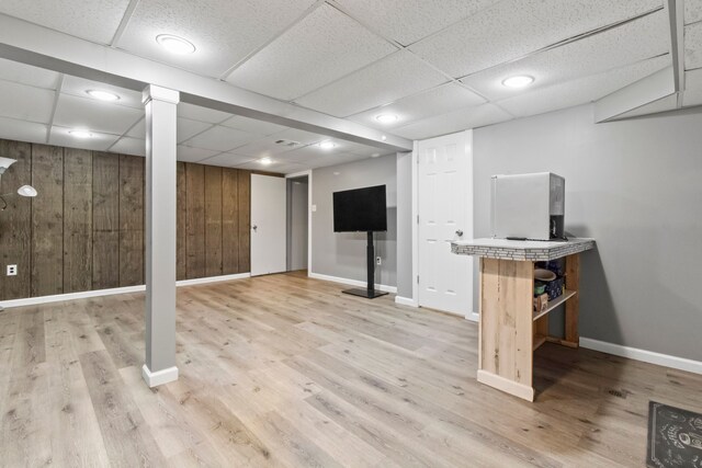 basement featuring a paneled ceiling, light hardwood / wood-style floors, and wood walls