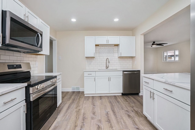 kitchen with sink, light stone counters, light wood-type flooring, stainless steel appliances, and white cabinets