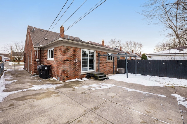 snow covered back of property with central AC and a patio area