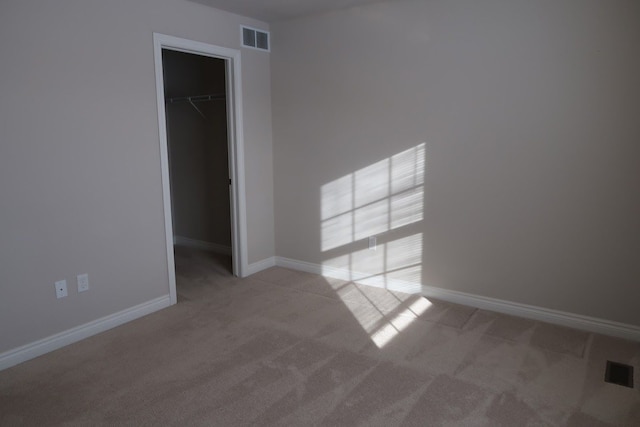 unfurnished bedroom with a walk in closet, light colored carpet, and a closet