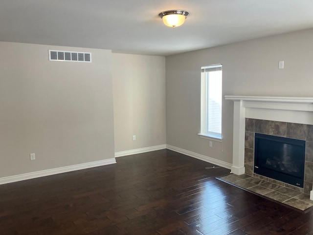 unfurnished living room with a tiled fireplace and dark hardwood / wood-style floors