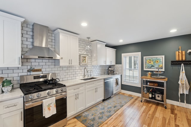 kitchen featuring appliances with stainless steel finishes, pendant lighting, sink, white cabinets, and wall chimney exhaust hood