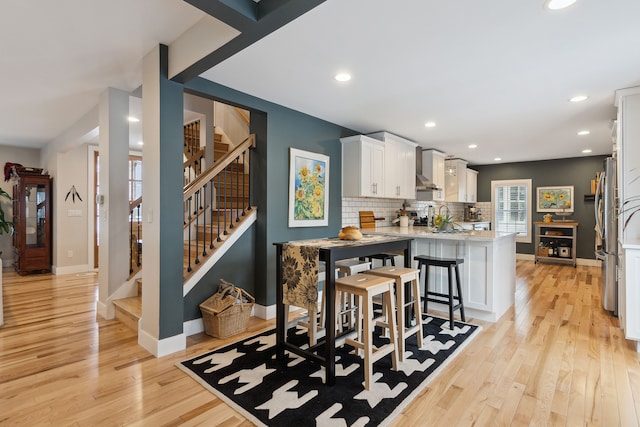 kitchen with a breakfast bar, white cabinetry, backsplash, light hardwood / wood-style floors, and kitchen peninsula