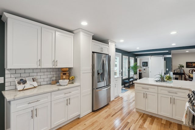 kitchen featuring stainless steel appliances, light hardwood / wood-style floors, white cabinets, decorative backsplash, and a barn door