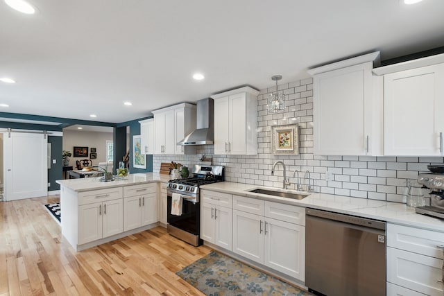 kitchen featuring wall chimney range hood, sink, stainless steel appliances, kitchen peninsula, and a barn door