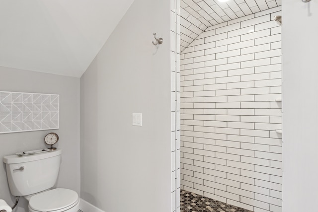 bathroom featuring lofted ceiling, toilet, and tiled shower