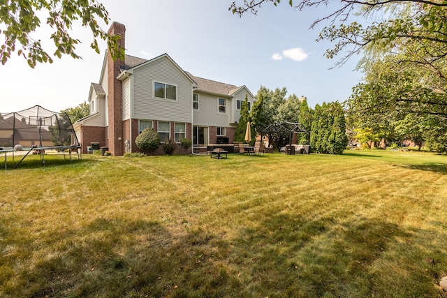 rear view of property featuring a trampoline, a gazebo, and a lawn