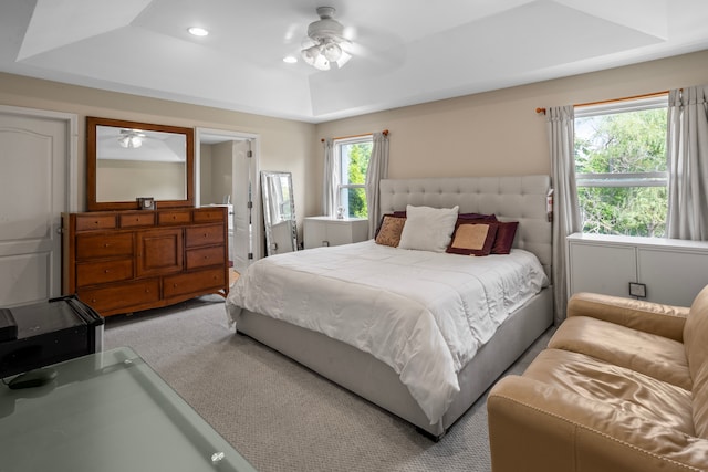 carpeted bedroom featuring ceiling fan, a tray ceiling, and multiple windows