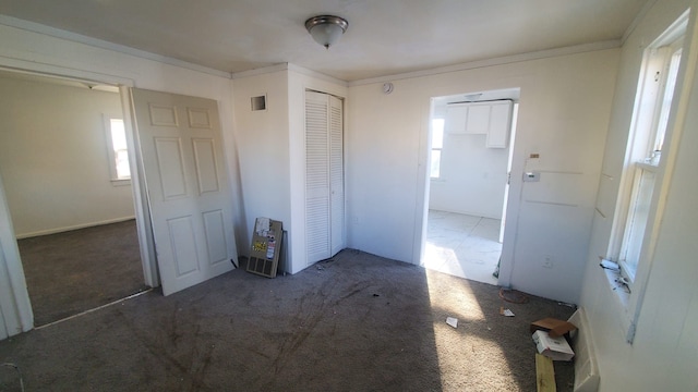 unfurnished bedroom with a closet, multiple windows, carpet, and crown molding