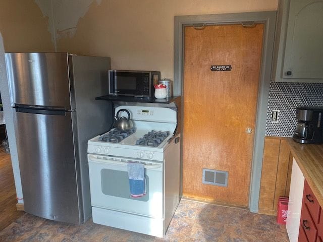 kitchen with stainless steel refrigerator, butcher block counters, white gas stove, and decorative backsplash