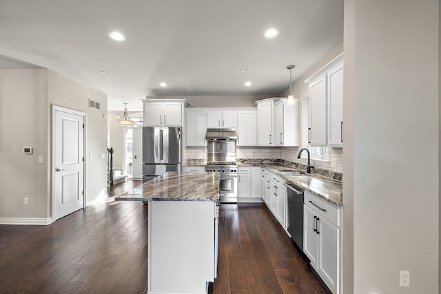 kitchen featuring sink, decorative light fixtures, dark stone countertops, a kitchen island, and stainless steel appliances