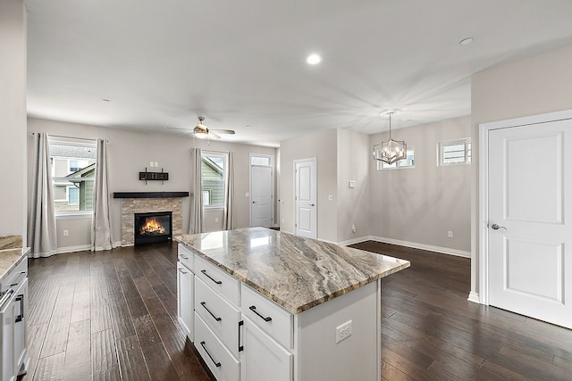 kitchen featuring dark wood-type flooring, white cabinetry, a center island, light stone counters, and decorative light fixtures