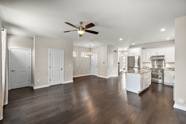 kitchen with a kitchen island, appliances with stainless steel finishes, white cabinets, dark hardwood / wood-style flooring, and light stone counters