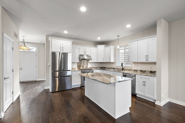 kitchen with white cabinetry, hanging light fixtures, a kitchen island, stainless steel appliances, and light stone countertops