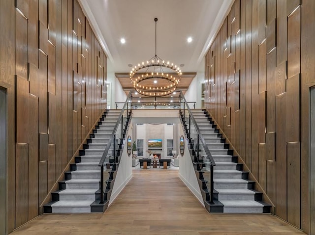 stairs with an inviting chandelier, wood-type flooring, and wooden walls