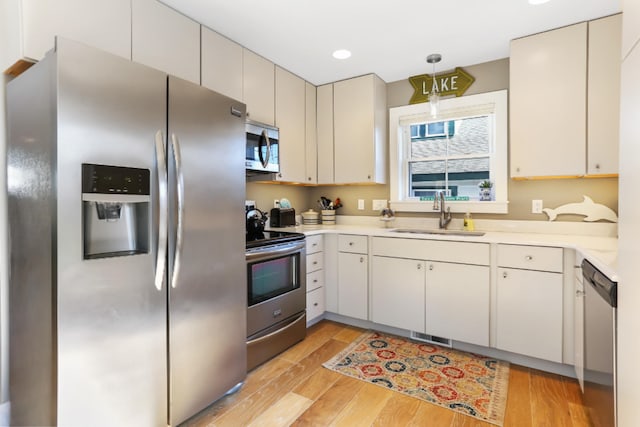 kitchen with pendant lighting, sink, stainless steel appliances, and light hardwood / wood-style floors