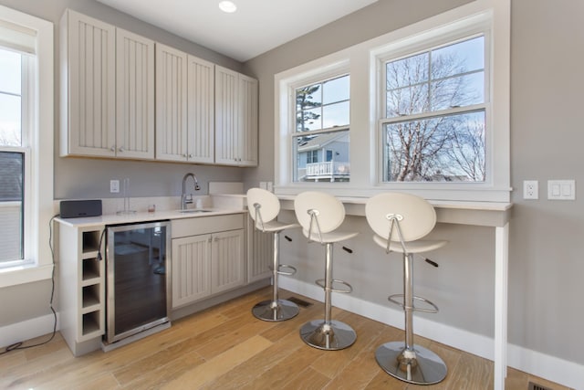 bar with sink, light hardwood / wood-style flooring, and beverage cooler