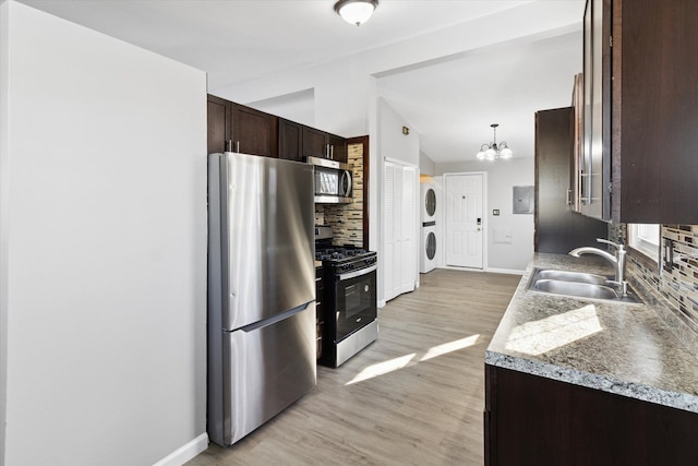 kitchen featuring appliances with stainless steel finishes, decorative light fixtures, tasteful backsplash, sink, and stacked washer / drying machine